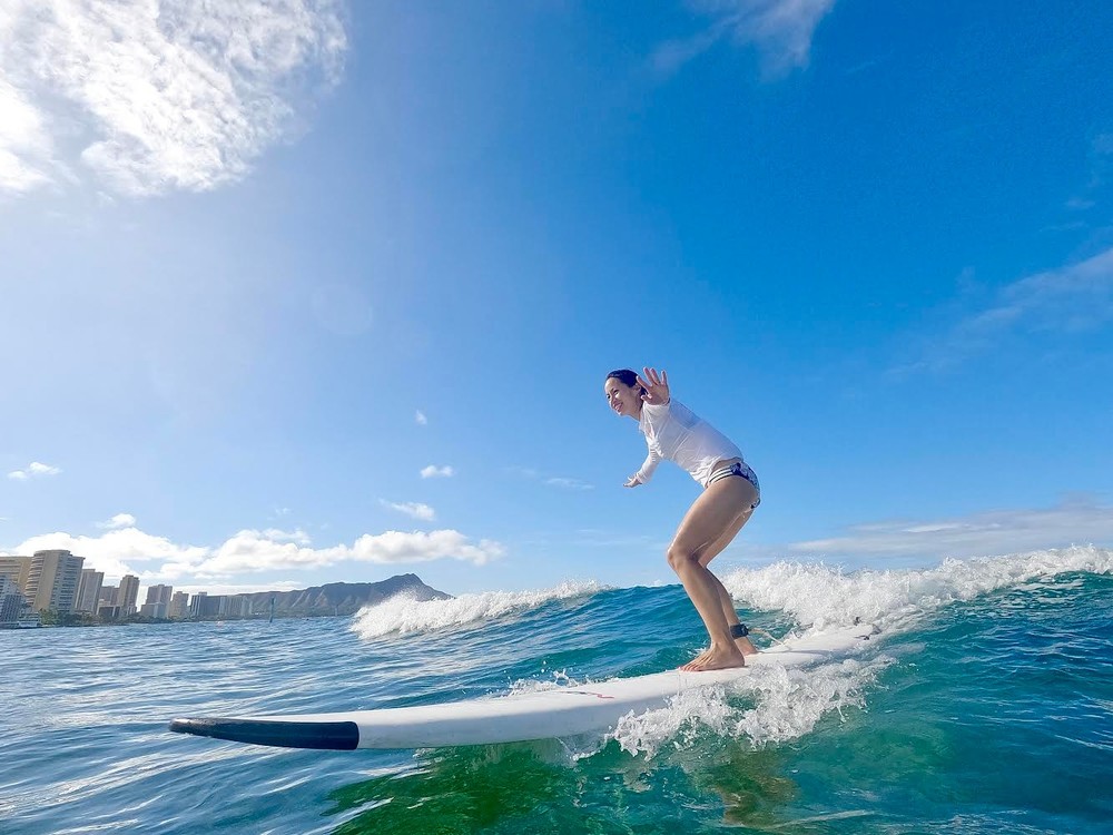 Lady wearing a white rash guard surfing on the ocean