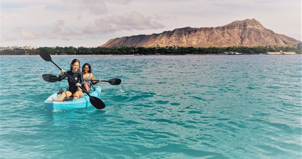 Two women paddling in a blue kayak on the ocean